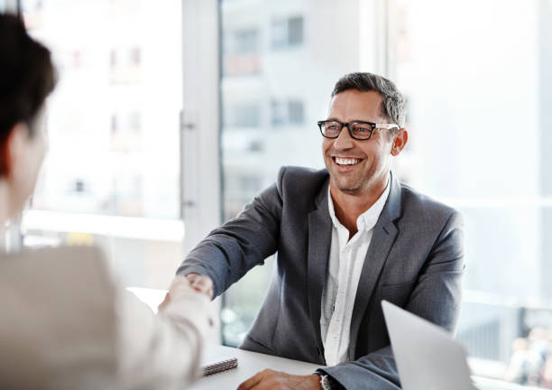 shot of two businesspeople shaking hands in an office shot of two businesspeople shaking hands in an office